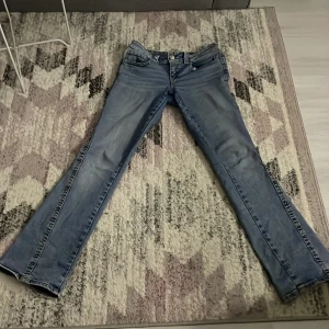 Gina tricot ljusblå bootcut jeans - Snygga ljusblå jeans från Gina tricot, (y2k low twisted bootcut jeans) med bootcut passform och låg midja. Jeansen har klassiska fem fickor, coola detaljer på bakfickorna med knappar och kontrastsömmar. Tillverkade i mjukt denim-material som sitter skönt och ger en avslappnad vibe.