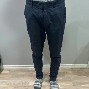 Mörkgrå kostymbyxor Massimo Dutti - Snygga mörkgrå kostymbyxor från Massimo Dutti i slim fit-modell. Byxorna har klassiska fickor, bälteshällor och en stilren look. Materialet är linneblandning som ger en skön känsla och lite struktur. Perfekt för dig som gillar en clean och modern stil. OBS!! Knapparna saknas till gylfen 