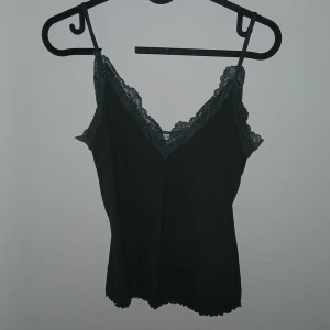 Grön linnetopp med spetskant - Snygg grönt  linnetopp med tunna axelband och v-ringning dekorerad med spetskant. Perfekt för att skapa en stilren och trendig look. Toppen har en figurnära passform och ärmlös design.