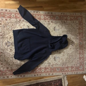 Mörkblå hoodie från Polo Ralph Lauren - Snygg mörkblå hoodie från Polo Ralph Lauren med klassisk röd broderad logga på bröstet. Tröjan har huva, magficka och långa ärmar. Tillverkad i mjuk bomull som är skön att ha på sig. Perfekt för dig som gillar stilrena och tidlösa plagg.