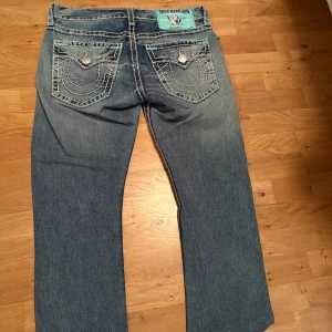 True Religion Ricky Super T jeans blå -   blå jeans från True Religion, modell Ricky Super T. De har kontrastsydda vita och turkosa sömmar, klassiska fem fickor med dekorativa knappar och detaljer på bakfickorna. Jeansen har rak passform och är tillverkade i slitstarkt denimtyg. Nypris på dessa var 5000kr, och dom finns inte tillgängliga längre plus att dom har börjat fadea lite i färgen så därav priset.