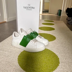 Valentino Garavani Open sneakers vit/grön - Gått ner från 2500kr-1750. Säljer ett par Valentino Garavani Open sneakers i vitt skinn med en bred grön rem över ovansidan. Skorna har platt sula, rund tå och coola nitar på hälen. Kommer med originalkartong och dustbag. Perfekt för dig som gillar lyxiga och stilrena sneakers.