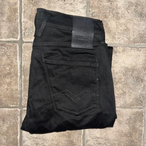 Replay Anbass Hyperflex jeans - Svarta Replay Anbass Hyperflex jeans med skinny passform och klassisk femficksdesign. Stretchigt material som sitter tajt och bekvämt. Snygga detaljer med svarta sömmar och Replay-logga på bakfickan. Midja 40cm, längd 106cm. JAG SKICKAR EJ FLER BILDER NÄR JAG BÄR JEANSEN! för storleksguide hänvisar jag till måtten och för bättre inblick i passformen rekommenderar jag att googla på modellnamnet. Jeansen kan vara uppsydda utan att jag noterat det så kolla måtten noggrant :) s4 