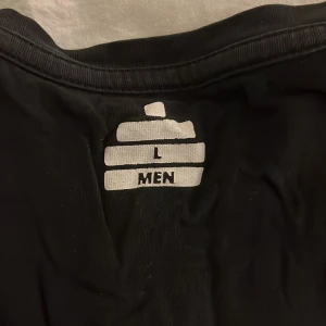 Svart t-shirt från Tyngre, storlek L - Svart t-shirt från Tyngre i storlek L med vit logotyp tryckt på bröstet. Klassisk rund hals och korta ärmar. Materialet känns mjukt och lätt, perfekt för dig som gillar enkel och stilren design. Passar dig som vill ha en clean look med sportig vibe.