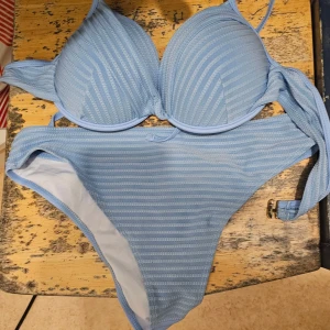Ljusblå randig bikini med snörning - Supersnygg ljusblå bikini med ränder och vadderad topp. Bikinin har snörning i sidorna på överdelen och klassisk bikiniunderdel. Perfekt för strandhäng och poolparty! Materialet känns mjukt och bekvämt mot huden.