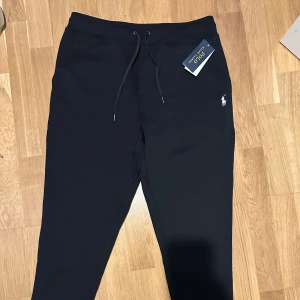 Svarta mjukisbyxor Polo Ralph Lauren M - Svarta mjukisbyxor från Polo Ralph Lauren med klassisk broderad logga på höften. Byxorna har dragsko i midjan och muddar vid bensluten för en skön passform. Perfekta för chill eller streetwear. Tillverkade i mjukt material för extra komfort.