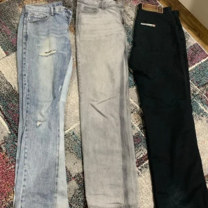 Tre par jeans i olika färger - Tre par jeans: ett ljusblått par med slitningar och hål, ett par i ljusgrå tvätt och ett par i svart med klassisk Levi's-lapp bak. Alla har raka ben och femficksmodell, perfekta för en avslappnad stil.