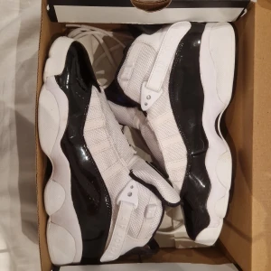 Nike Air Jordan 6 Rings svart/vit - Nike Air Jordan 6 Rings sneakers i svart och vitt med glansig svart lackdetalj, vit mesh och klassisk Jumpman-logga i lila på plösen. Snygg och chunky sula med lila detaljer undertill. Skorna har snörning och coola detaljer som gör dem till ett statement.