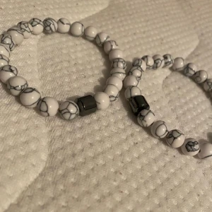 Vita marmorerade pärlarmband - Två snygga armband med vita pärlor och grå marmorerade detaljer. Armbanden har en cool metallisk pärla i mitten som ger extra edge. Perfekt accessoar för att lyfta din stil med en unik touch. Helt nya finns andra färger oxå!!