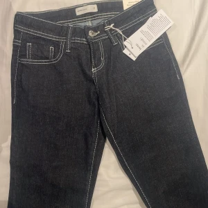 Mörkblå bootcut jeans med kontrastsömmar - Snygga mörkblå jeans från Perfect Jeans med tydliga vita kontrastsömmar. Modellen har klassisk femficksdesign och bootcut-ben som ger en schysst siluett. Jeansen är tillverkade i jeansmaterial och har knapp och dragkedja framtill.