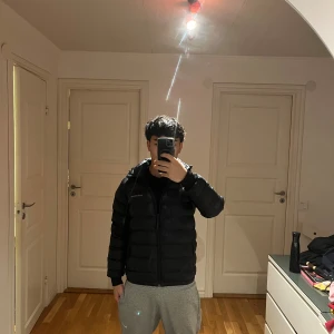 Svart dunjacka Peak Performance 170 - Säljer en svart dunjacka från Peak Performance i storlek 170. Jackan har en klassisk pufferstil med huva, dragkedja framtill och diskret logga på bröstet. Perfekt för kalla dagar och riktigt snygg till streetwear-looken. Har lite hål på båda armarna och en vid magen men syns inte mycket