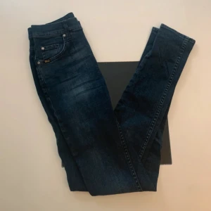 Mörkblå jeans Tiger of Sweden Kelly - Snygga mörkblå jeans från Tiger of Sweden i modellen Kelly. Klassisk femficksdesign med silverfärgade nitar och diskret logga vid fickan. Jeansen har en rak passform och är tillverkade i mjukt denimtyg som sitter skönt hela dagen.