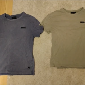 Två GNMD t-shirts i blått och beige - Säljer två stilrena t-shirts från GNMD, en i dämpad blå och en i beige. Båda har korta ärmar, rund hals och liten logotyp på bröstet. Materialet är mjuk bomull som känns skönt mot huden. Perfekt för dig som gillar enkel och clean stil.