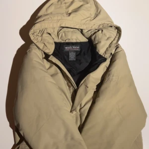 Beige dunjacka från Woolrich XL - Säljer en beige dunjacka från Woolrich i storlek XL. Jackan har huva, flera fickor med knappstängning och dragkedja framtill. Yttermaterialet är nylon och fodret är dunfyllt för extra värme. Perfekt för kalla dagar och har en clean, klassisk look.