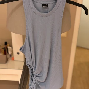 Ljusblå ribbad linnetopp Gina Tricot - Säljer en ljusblå ribbad linnetopp från Gina Tricot i storlek M. Toppen är ärmlös med rund halsringning och har snygg snörningsdetalj på sidan som ger en cool twist. Perfekt för dig som gillar stilrena och trendiga plagg.