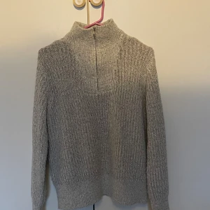 Grå stickad polotröja från Object - Mysig grå stickad polotröja från Object med lång ärm och half zip-dragkedja i halsen. Tröjan har en chunky ribbstickad struktur och hög krage som ger en cool vibe. Perfekt för lager-på-lager under kyliga dagar.