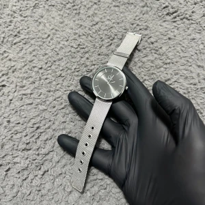 Silverfärgad Calvin Klein klocka - Stilren klocka från Calvin Klein med rund urtavla i silver och minimalistiska markeringar. Armbandet är i meshad rostfri stål och har justerbara hål för perfekt passform. Snygg och modern design som lyfter din outfit.