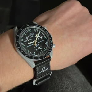 Omega x Swatch Speedmaster Moonswatch - Säljer en Omega x Swatch Speedmaster Moonswatch med svart urtavla, grå boett och svart band med Omega-logga. Klockan har tachymeter-skala, flera subdials och tydliga vita detaljer. Bandet är syntetmaterial och har Speedmaster-tryck på insidan. Klockan har kronograf funktionen! Priset satt då jag inte har orginal förpackningen!