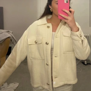 Oversized vit overshirt med fickor - Säljer en oversized vit overshirt med stora bröstfickor och guldfärgade knappar. Jackan har klassisk krage och lång ärm med knapp vid mudden. Materialet är mjukt och har en lätt struktur som ger en chill vibe. Perfekt att slänga över en t-shirt för en clean look.