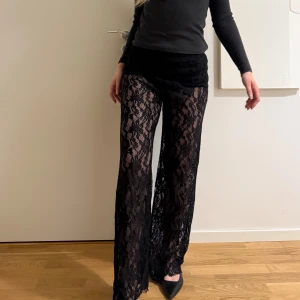Svarta spetsbyxor  - Säljer ett par svarta byxor i transparent spets med blommönster. Byxorna har hög midja och ett loose fit med raka ben. Materialet är mjukt och stretchigt, vilket gör dem riktigt bekväma och snygga. Perfekta för dig som vill sticka ut med en unik stil.