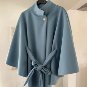 Blå poncho /jacka med bälte och knapp - Snygg ljusblå poncho /jacka med breda ärmar och högt krage. Kappan har ett bälte i midjan som knyts framtill och en guldfärgad knapp vid halsen. Stilren och minimalistisk design, perfekt för dig som gillar klassiska plagg med en modern twist.