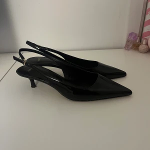 Svarta pumps med spetsig tå från Mango - Snygga svarta pumps från Mango med spetsig tå och låg klack. Skorna har en elegant design med justerbart spänne och är tillverkade i blankt material. Perfekta för dig som gillar stilrena och trendiga skor. Pris kan diskuteras vid snabb affär. 