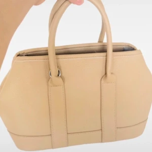 Beige handväska i skinn med dragkedja - Stilren beige handväska i skinn med två rejäla handtag och avtagbar axelrem. Väskan har en klassisk form och stängs med dragkedja upptill. Perfekt för dig som vill ha en enkel men snygg accessoar till vardagslooken. Helt ny och köpt för ett dyrt pris. Man kan få med ett rem till väskan. 