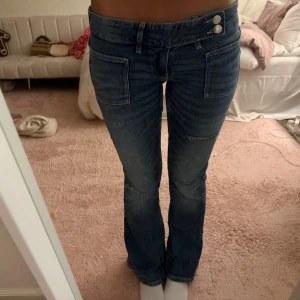 Blå bootcut jeans med dubbla knappar - Säljer ett par blåa lågmidjade oanvända Gina Tricot jeans. Meddela för mer bilder eller mått eller om ni vill diskutera pris!