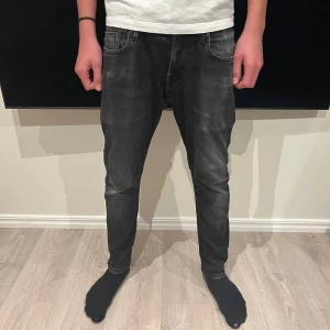 Svarta jeans från G-Star RAW - Säljer ett par svarta jeans från G-Star RAW med snyggt tvättad look och klassiska fem fickor. Jeansen är slim fit och normal passform, med detaljerade bakfickor och logopatch i midjan. Perfekta för dig som gillar en stilren och modern vibe.