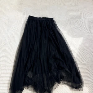 Svart lång tyllkjol från SHEIN - Svart långkjol från SHEIN i storlek S. Kjolen är gjord i flera lager tunn tyll som ger en snygg volym och flowig känsla. Resår i midjan för skön passform. Perfekt för dig som vill ha en dramatisk och trendig look.