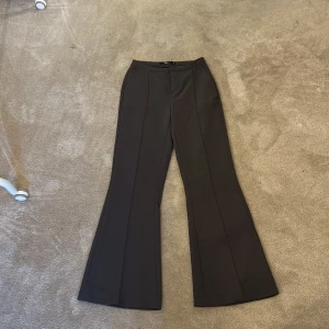 Mörkgrå bootcut kostymbyxor Gina Tricot - Snygga svarta kostymbyxor från Gina Tricot i bootcut-modell. Byxorna har hög midja, pressveck framtill och fickor i sidorna. Perfekta för en clean och stilren look.