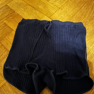 Mörkblå ribbade shorts från Sun Child - Mörkblå shorts från Sun Child i 100% bomull med ribbad struktur och snörning i midjan. De har en loose passform och är perfekta för varma dagar. Tillverkade i Tunisien.