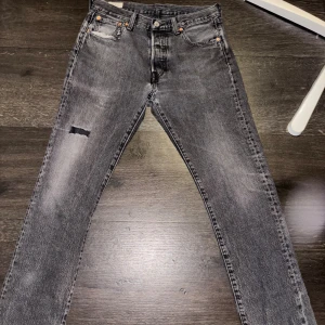 Levi's 501 grå jeans med slitningar - Säljer ett par Levi's 501 jeans i tvättad grå färg. Knappgylf, slitningar lite överallt och ett litet hål som syns på bild 5, tveka inte och höra av dig, pris kan diskuteras😊😊