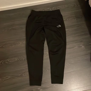 Svarta mjukisbyxor från The North Face - 👖 Svarta North Face mjukisbyxor – chill & träning! Säljer mjuka North Face-byxor med logga på benet. Slim passform, elastisk midja och ribbade muddar vid bensluten. Perfekta för både chill och träning, tillverkade i mjukt syntetmaterial som känns skönt mot huden 👟  💰 Pris: 350 kr