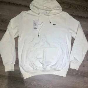 Lacoste Hoodie  - Säljer denna stilrena, nya och riktigt snygga vita Lacoste hoodien, passar perfekt till allt, dock är den liten i storleken, står XL men passar (M-L), skriv gärna vid intresse och för mer information! 