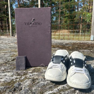 Valentino Garavani sneakers vit/svart 42 - Säljer ett par Valentino Garavani sneakers i vitt skinn med svart detalj över vristen och coola nitar på hälen. Klassisk rund tå, vita snören och platt sula. Snygg och stilren design som sticker ut med den svarta kontrasten.
