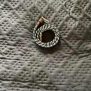 Randigt flätat bälte med läderdetaljer - Säljer ett snyggt randigt bälte i svart och vitt med flätad design. Bältet har bruna läderdetaljer vid spännet som ger en schysst kontrast. Perfekt accessoar för att lyfta din outfit med en cool touch.