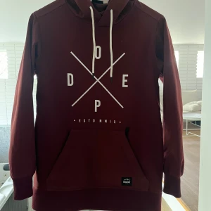 Vinröd hoodie från Dope med tryck - Snygg vinröd skidjacka/hoodie från Dope. Jackan har huva med vita snören och ribbade muddar. Perfekt i skidbacken.