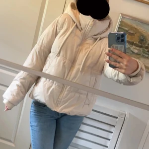 Beige pufferjacka från Zara XS - Säljer en beige pufferjacka från Zara i storlek XS. Jackan har huva, dragkedja framtill och snörning vid halsen. Den är vadderad och har en oversized vibe, perfekt för kalla dagar. Enkel och stilren design som passar till jeans eller andra outfits.