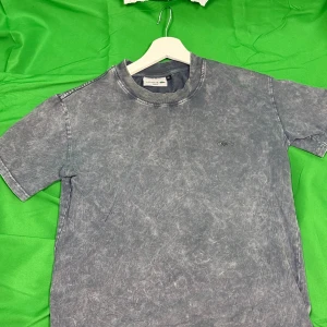 Grå  t-shirt från Lacoste - Snygg grå t-shirt från Lacoste med  effekt och klassisk krokodillogga på bröstet. T-shirten har rund halsringning och korta ärmar. Tillverkad i mjuk bomull för en skön känsla och avslappnad stil.Liknande modell som originalet!
