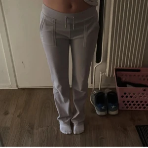 Ljusgråa mjukisbyxor Juicy Couture - Säljer ett par gråa mjukisbyxor från Juicy Couture med bred resår i midjan och snörning framtill.  tillverkade i mjuk velour - Perfekta för en chill och avslappnad stil.