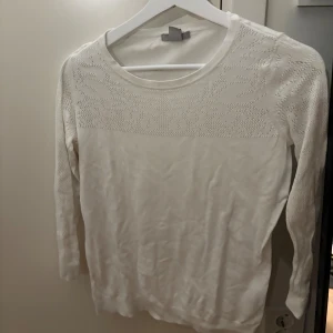 Vit stickad tröja från H&M, M - Säljer en vit tröja från H&M i storlek M. Tröjan har ett diskret hålmönster upptill och långa ärmar. 