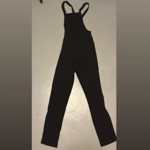 Svart byxdress H&M  - Snygga dragkedjor i sidorna ger en cool detalj. Tillverkad i ett mjukt tyg som känns skönt mot huden. Perfekt för dig som gillar enkel men stilren look. 