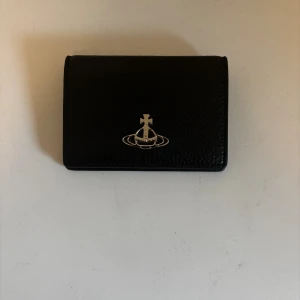 Vivienne Westwood korthållare/plånbok - En Vivienne Westwood korthållare/plånbock med 4 fack där ett av dem är ett genomskinligt för id. Väldigt bra skick och knappast använt, det finns en liten fläck på id facket vilket du kan se på bilderna men den påverkar knappt synligheten av ett id. Made in Italy och Kvitto finns samt om ni har frågor är det bara att kontakta mig.