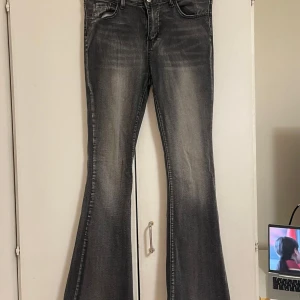 Grå bootcut jeans med slitningar - Snygga grå-svarta jeans med bootcut-modell och coola slitningar framtill. Jeansen har klassisk femficksdesign, dragkedja och knapp i midjan. Materialet är jeans med en tvättad look. Perfekta skick däremot så finns det en jätte liten vit fläck som man inte ser om man inte kollar jätte noggrant, den kom till mig på de så. 