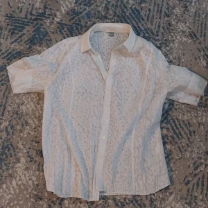 Beige leopardmönstrad skjorta från ERFO - Snygg beige skjorta från ERFO med diskret leopardmönster i grått. Skjortan har korta ärmar, klassisk krage och knäppning framtill. Tunt och luftigt material som passar perfekt till varmare dagar.