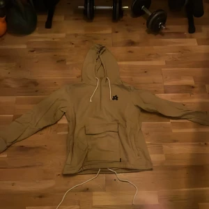 Beige hoodie Golf Le Fleur Converse XS - Säljer en beige hoodie från Converse x Golf Le Fleur med huva och snörning. Stor magficka framtill, tryckt blomma på bröstet och text på ryggen. Skön passform och tillverkad i mjuk bomull. Perfekt för dig som gillar streetwear och snygga detaljer.