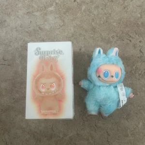 Labubu - Bilderna visar en Surprise Baby vinyl plush pendant blind box med en blå plyschfigur (modell 'Hope'). Produkten är i mycket fint skick och levereras med originalförpackning. Perfekt som samlarobjekt eller present. Inga synliga defekter eller slitage.