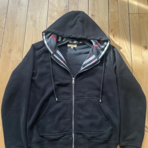 Svart hoodie från Burberry med dragkedja - Storlek M passar storlek S också liten i storleken. Tröjan har hel dragkedja. Tillverkad i mjuk och varm bomull, perfekt för höst och vinter.