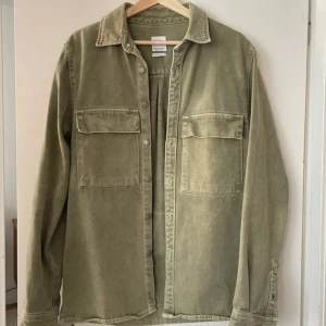 Grön overshirt från zara - Snygg relaxed fit overshirt från Zara i en dämpad grön färg. Tillverkad i mjuk bomull med två stora bröstfickor och knappar framtill. Långärmad modell med klassisk krage och detaljer vid ärmslut. Perfekt att slänga på över en t-shirt.